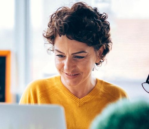 Woman in yellow sweater smiling while looking at laptop